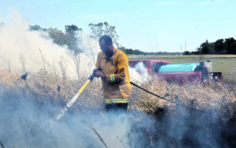 Municipal firefighter using foam sprayer near grass fire